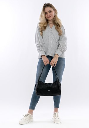 Schwarze Lederhandtasche mit weicher, runder Form und einer dezent strukturierten Oberfläche. Das Modell trägt ein gestreiftes Oberteil und blaue Jeans.