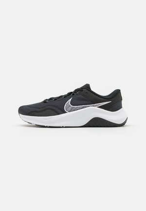Black athletic shoe with a mesh upper and white accents. Features a rounded toe, flat laces, and a textured black rubber sole.