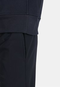 Felpa blu navy con bordo e polsini a coste, abbinata a pantaloni blu navy con tasche laterali e una texture liscia.