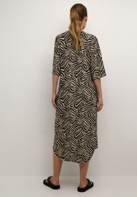 Robe longue et ample couleur beige avec des rayures abstraites zèbre noires. Elle présente des manches trois-quarts et un ourlet arrondi, fabriquée en tissu doux.