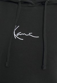 Felpa nera con cappuccio realizzata in tessuto morbido, caratterizzata da un design con firma ricamata in bianco. Sono presenti dei lacci al collo.
