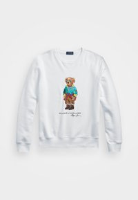 Sudadera blanca con cuello redondo y puños de canalé que presenta un oso colorido bordado que lleva una chaqueta azul y gafas de sol.