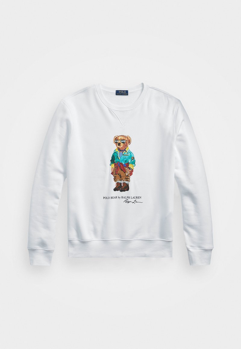 Sudadera blanca con cuello redondo y puños de canalé que presenta un oso colorido bordado que lleva una chaqueta azul y gafas de sol.