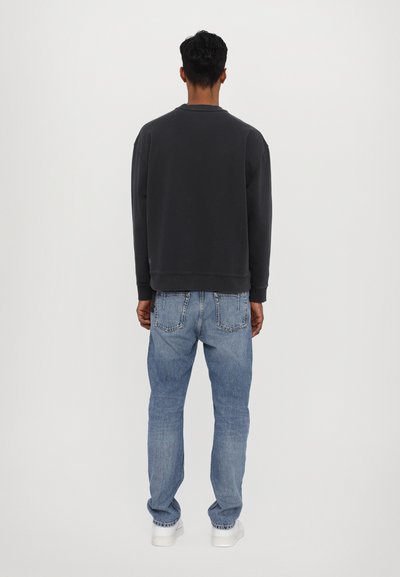 Sweatshirt gris foncé avec un col rond, associé à un jean bleu clair. La tenue présente une coupe décontractée et des éléments de design minimalistes.