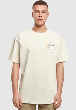 Lys beige oversized t-skjorte laget av bomull, med et tegneserie-spøkelse grafikk og "Boo to You" tekst i oransje på venstre brystområde.