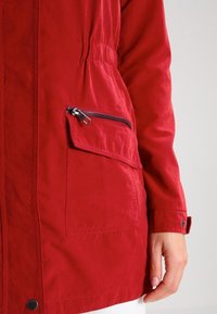 Röd lättviktsjacka med slät yta, ficka med dragkedja på sidan, elastisk midja och knappade ärmar. Skräddarsydd design med modern passform.