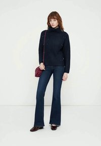 Tumši zils, ribots augsta kakla džemperis ar rotājumiem, kopā ar tumši zilām zvana biksēm un mazu sarkanu krūšu somiņu.