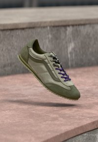 Baskets vert olive et beige avec des lacets mélangés, une paire noir et blanc et une violette, flottant au-dessus de marches en pierre.