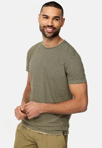Kortærmet t-shirt i tan med et struktureret geometrisk mønster. Har en rund halsudskæring og en afslappet pasform. Let stof, afslappet design.