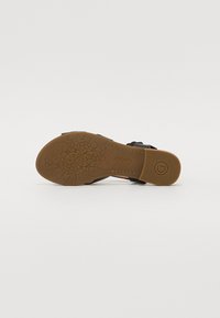 Black sandal with a textured brown rubber sole featuring floral patterns. Design includes two adjustable straps for a secure fit.