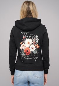Black hoodie with a floral design featuring roses and white flowers. Text reads "Good Things Are Coming" in a handwritten font.