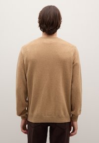 Hellbrauner Pullover aus weichem Stoff mit rundem Ausschnitt, langen Ärmeln sowie gerippten Bündchen und Saum. Kombiniert mit dunkelbraunen Hosen.