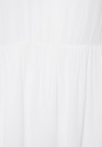Tissu blanc avec une texture plissée et des lignes verticales subtiles, froncé à une couture horizontale créant un design en étages.