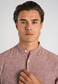 Camicia a maniche corte con colletto in un tessuto di un marrone rossastro chiaro con finitura texturizzata. Presenta una chiusura con bottoni e una vestibilità rilassata.