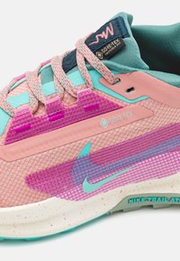Des baskets Nike avec une tige en mesh rose et des accents turquoise, des superpositions texturées violettes et une semelle intermédiaire crème à veines. La marque GORE-TEX est visible.