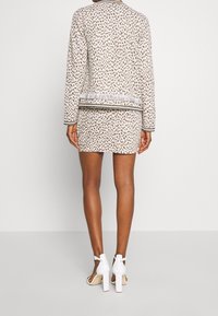 Valkoinen takki ja hame -setti ruskealla leopardikuosisella, reunustamisen yksityiskohdalla helmassa ja kontrastivärisellä mustalla kammalla. Yhdistetty valkoisiin korkokenkiin.