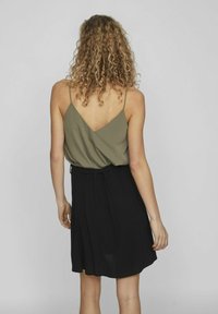 Olivgrön ärmlös topp med V-back, kombinerad med en svart plisserad kjol. Outfiten har tunna axelband och en avslappnad passform.