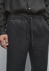 Zwarte linnen broek met een elastische tailleband en een trekkoord. Beschikt over een relaxte pasvorm en subtiele textuur, aangevuld met een bijpassend shirt.