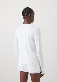 White long-sleeve top made of lightweight fabric, featuring a crew neck and fitted design. Paired with white shorts, smooth texture.