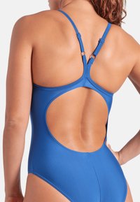 Niebieski jednoczęściowy kostium kąpielowy z wycięciem na plecach. Posiada regulowane ramiączka oraz gładką, matową fakturę. Udekorowany metalowymi akcentami.