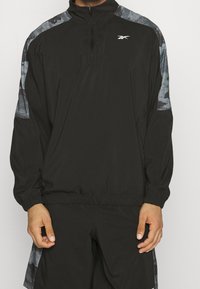 Sudadera negra con media cremallera en el cuello, con detalles en gris con patrón en los hombros y puños elásticos para un ajuste ceñido.