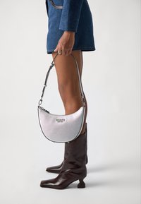 Borsa a mezzaluna argento con finitura testurizzata, rifiniture nere e tracolla corta. Logo impressa sul davanti. Stivali neri con tacco in cornice.