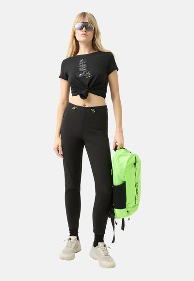Black cropped t-shirt with a knotted front and graphic design. Slim-fit black pants with green accents. Bright green backpack with logo.