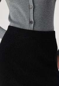 Ribbed grå cardigan med knappstängning, i kombination med en svart ribbad kjol. Båda har textil i strukturerad design och en figurnära passform.