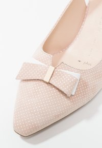 Chaussure plate rose clair à bout pointu avec des pois blancs. Présente un accent nœud à l'avant avec un détail en métal doré. Texture en daim douce.