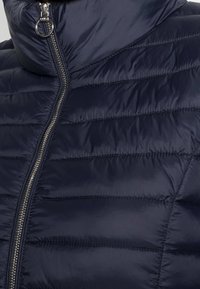 Giacca puffer blu navy con design a cuciture orizzontali, colletto alto e zip metallica. Texture liscia e lucida con una forma moderna e aderente.
