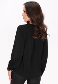 Blusa nera a maniche lunghe con vestibilità rilassata, caratterizzata da un colletto rotondo e maniche arricciate. Tessuto liscio, design semplice, senza decorazioni.