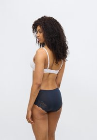 Λευκό σουτιέν με ρυθμιζόμενες τιράντες συνδυασμένο με σκούρες μπλε, ψηλόμεσες σλιπ με λουλουδένιες δαντελένιες λεπτομέρειες στα πλάγια. Λείο υλικό.