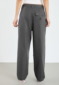 Dunkelgraue weite Hosen mit einer Gesäßtasche und Knopfdetails, aus einem glatten Material gefertigt, mit einem hüfthohen Bund.
