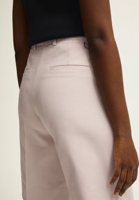 Jasnoróżowe, dopasowane spodnie z gładkiego materiału, z tylnymi kieszeniami i szlufką na pasek, połączone z czarnym, prążkowanym topem.