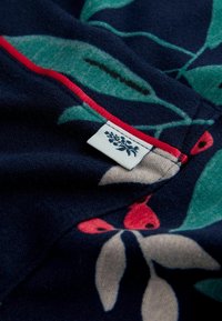 Námořnická fleecová tkanina s designem zelených listů a červených bobulí, se kontrastním červeným švem a malou nálepku na okraji.