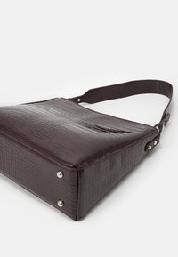 Tumma ruskea krokotiilikuviollinen käsilaukku kiiltävällä viimeistelyllä, suorakaiteen muotoinen, säädettävä olkahihna ja hopeanväriset metalliosat.