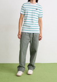 Pruhované tričko s krátkým rukávem v bílé, zelené a modré barvě s logem Nike; kombinováno s volnými šedými kalhotami a bílými teniskami.