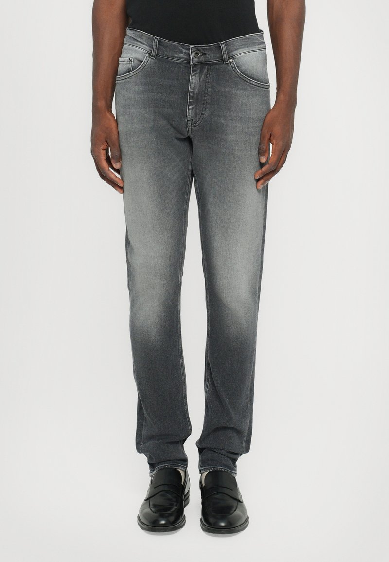 Szürke farmernadrág slim fit szabással, enyhe kopással, négy zsebbel és cipzáros zárással. Fekete bőr mokaszinokkal párosítva.