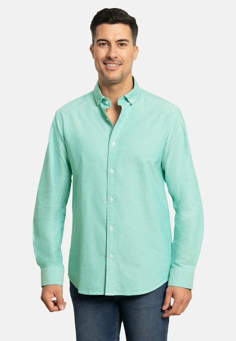 Camisa abotonada de color azul claro con mangas largas, con cuello abotonado y una textura sutil, combinada con jeans oscuros.