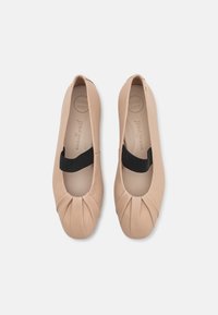 Ballerines en cuir nude avec un bout rond, un détail plissé à l'avant et une bande élastique noire sur le cou-de-pied. Intérieur très doux.