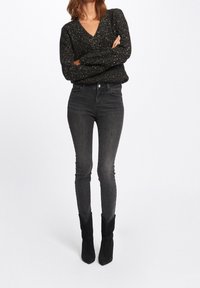 Black, sparkly knit sweater with a v-neck, paired with dark gray skinny jeans and black, pointed toe ankle boots. Simple, fitted design.