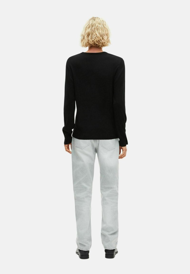 Haut noir à manches longues avec un col arrondi, associé à un jean droit gris clair. Texture lisse et design décontracté.