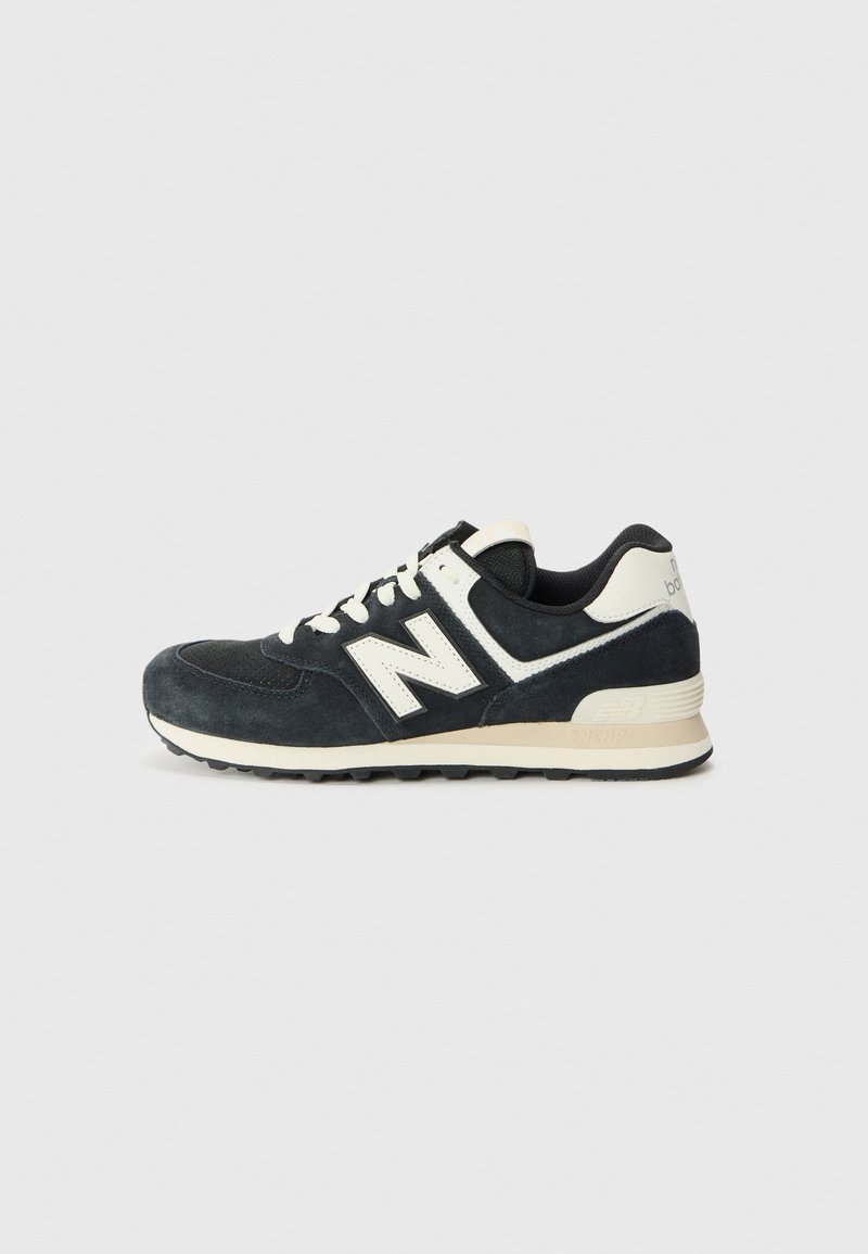 Baskets New Balance noir et blanc avec empeigne en daim, logo "N" blanc, lacets blancs et semelle beige sur fond clair uni.