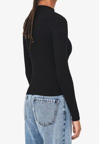 Top nero a maniche lunghe con coste e collo alto, design aderente. Abbinato a jeans a vita alta di colore azzurro chiaro con tasche posteriori.