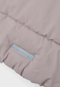 Dettaglio di un morbido piumino rosa chiaro con una texture liscia e lucida, e un'etichetta sintetica blu con scritte in rilievo.
