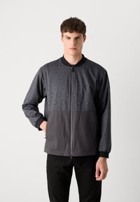 Men's jacket in dark gray with a hexagonal pattern on the upper section. Features a zip front and black ribbed collar and cuffs.