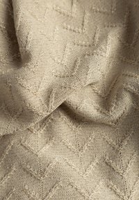 Beżowa tkanina o fakturze, z motywem w zygzak z subtelnymi metalicznymi włóknami, tworzącymi wypukły wzór. Miękki i elastyczny materiał.