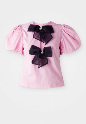 Rosa kortermet bluse med puffede ermer og to store svarte sløyfer med dekorative midtpunkter på forsiden.