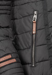 Zwarte pufferjack met gequiltte textuur, zilveren ritssluiting en een bruin leren label met de merknaam. Accenten zijn onder andere stiksels en zakken.