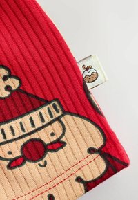 Roter gerippter Stoff, der ein Santa-Gesicht darstellt, mit einem beigen unteren Teil. Auffällige Details sind ein Etikett mit einer Abbildung von einem Dessert.